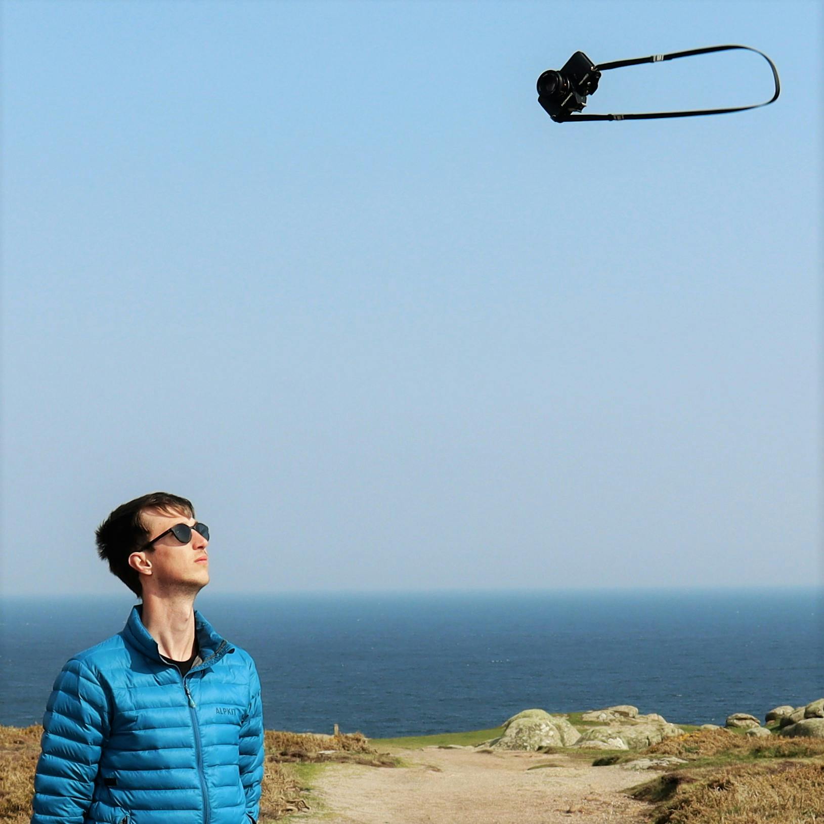 Person wearing sunglasses stares into the sky where a camera is floating